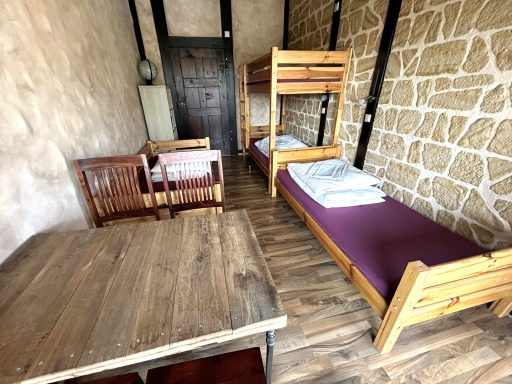 Zimmer mit zwei Einzelbetten, Tisch und Stühlen, Holzfußboden, steinerne Wand.