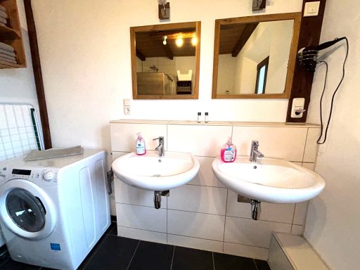 Zwei Waschbecken mit Spiegeln, Waschmaschine und Fön in einem Badezimmer.
