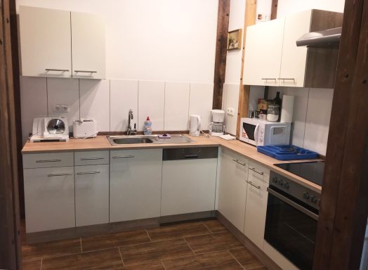 Moderne Küche mit weißen Möbeln, Holzdetails und Geräten wie Herd und Mikrowelle.