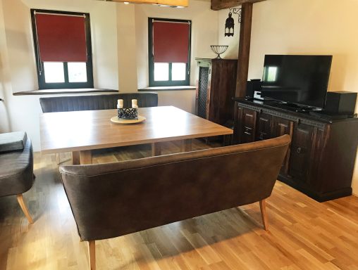 Ein wohnlicher Raum mit Holztisch, Stühlen, Fernseher und einem gemütlichen Sofa.