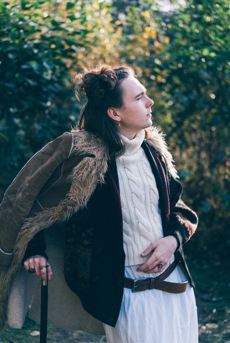 Aramis stützt sich auf einen Gehstock und ist in vielen Schichten gekleidet. Er blickt auf den Horizont.