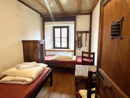 Historischer Schlafraum mit Holzmöbeln, zwei Betten und einem kleinen Tisch.