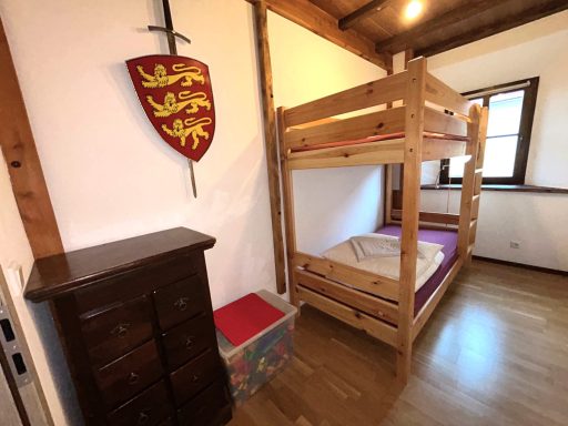 Hochbett in einem Zimmer mit einem Wappen und einer Kommode aus Holz.
