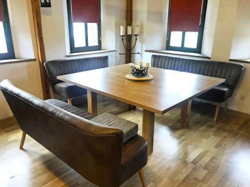 Holztisch mit Kerzenständer, umgeben von zwei Ledersofas in einem hellen Raum.