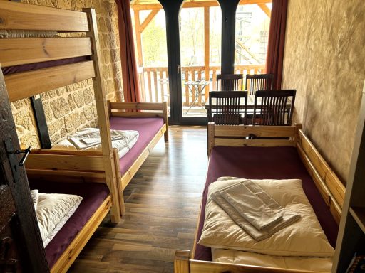 Zwei Etagenbetten mit Bettzeug in einem Holzraum mit Fenster und Stühlen.