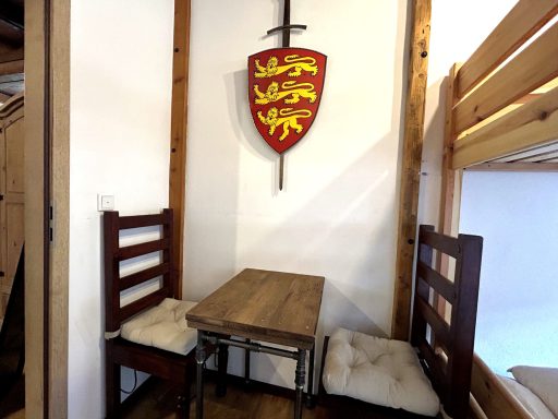Holztisch mit zwei Stühlen und einem Wappen an der Wand in einem gemütlichen Raum.