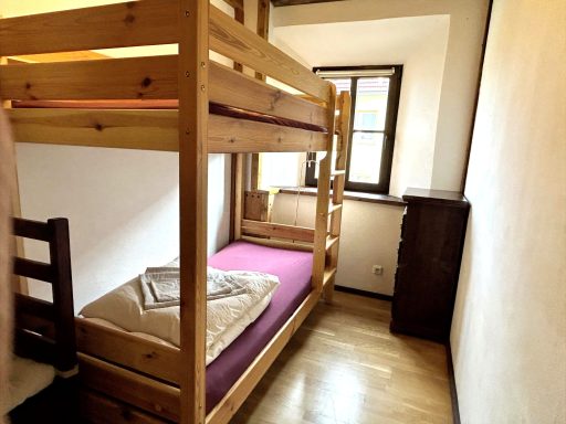 Kleines Zimmer mit Etagenbett, Holzkommode und Fenster.