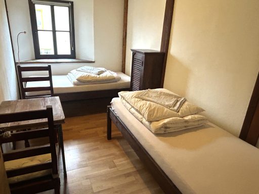 Ein einfaches Zimmer mit zwei Einzelbetten, einem Tisch und einem Fenster.